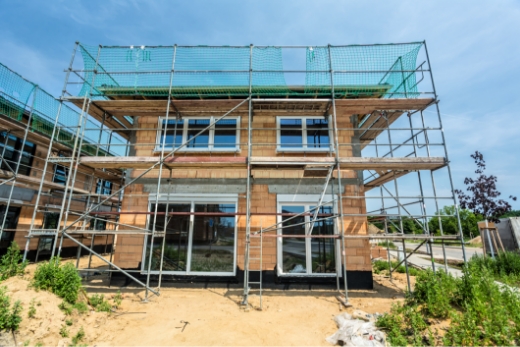 Ein im Bau befindliches zweistöckiges Haus mit Gerüsten und Sicherheitsnetzen umgeben.